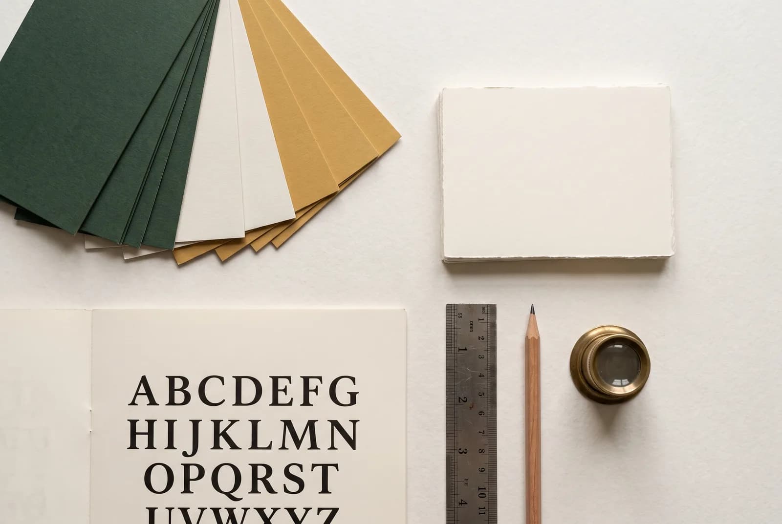 Papiers de couleur, cartes vierges, spécimen typographique, règle et compte-fils posés sur une table.